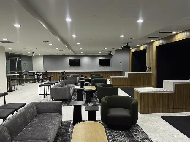 Modern lounge area with sofas, chairs, and tables under bright ceiling lights.