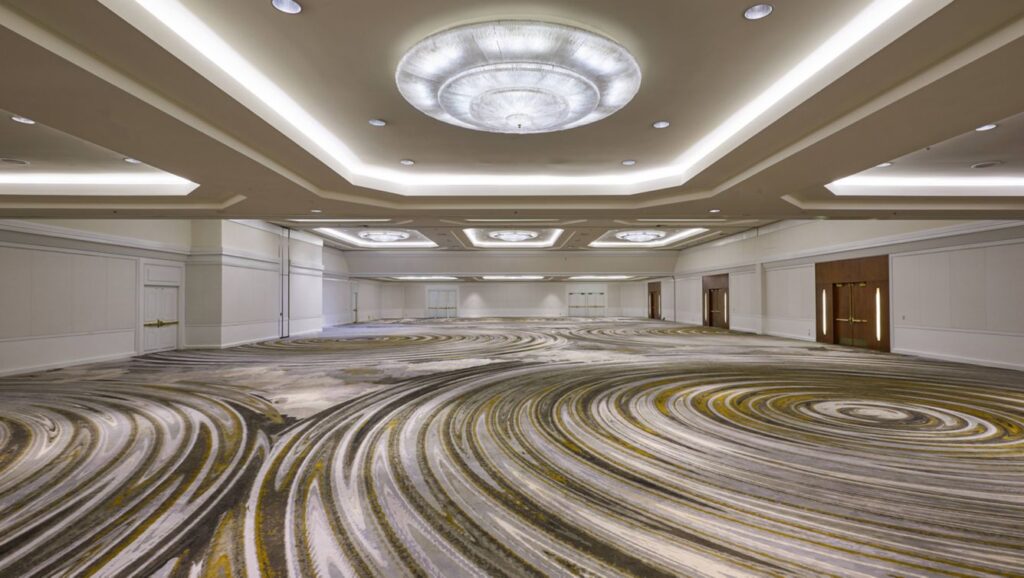 A large empty conference hall with modern lighting and patterned carpet.