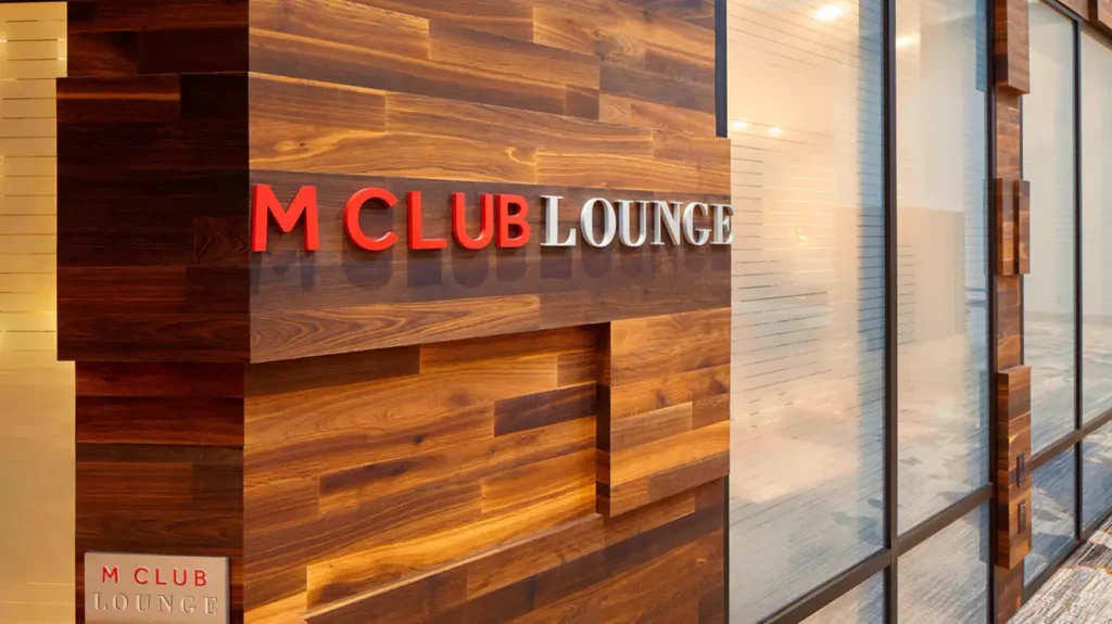 Wood-paneled wall with 'M CLUB LOUNGE' sign in red and white letters.