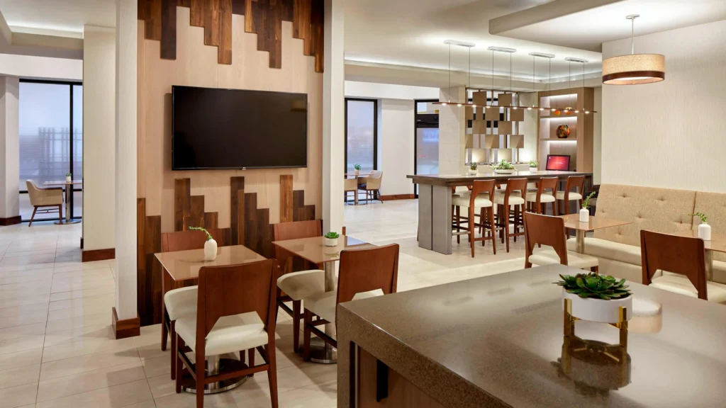 Modern dining area with wooden chairs and a large TV on the wall.