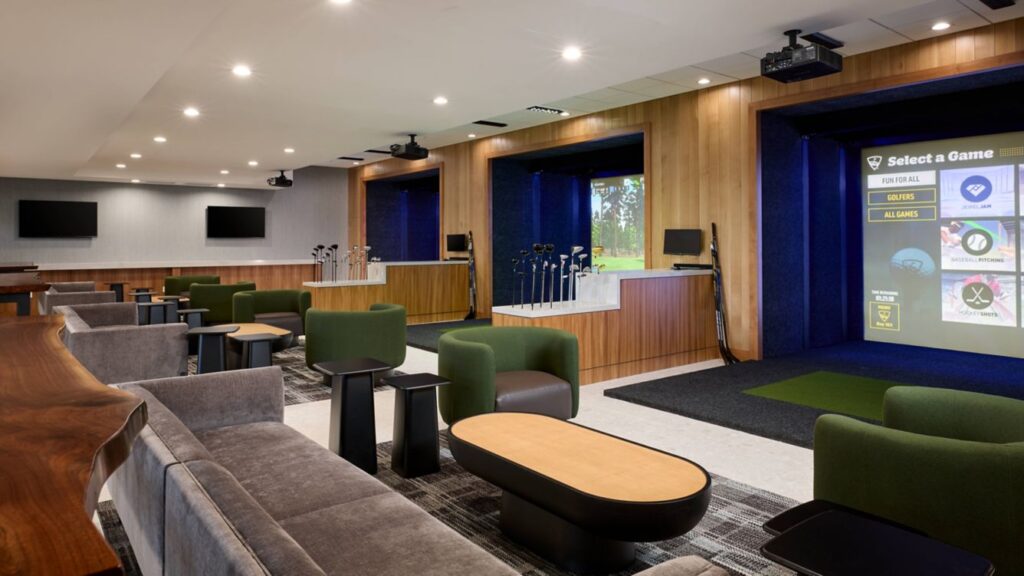 Modern indoor golf simulator room with seating and wood paneling.